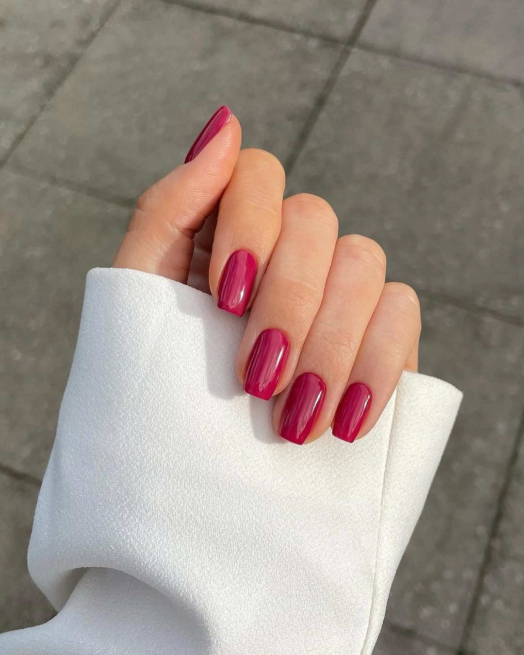 Glossy berry magenta squared nails beside white sleeve
