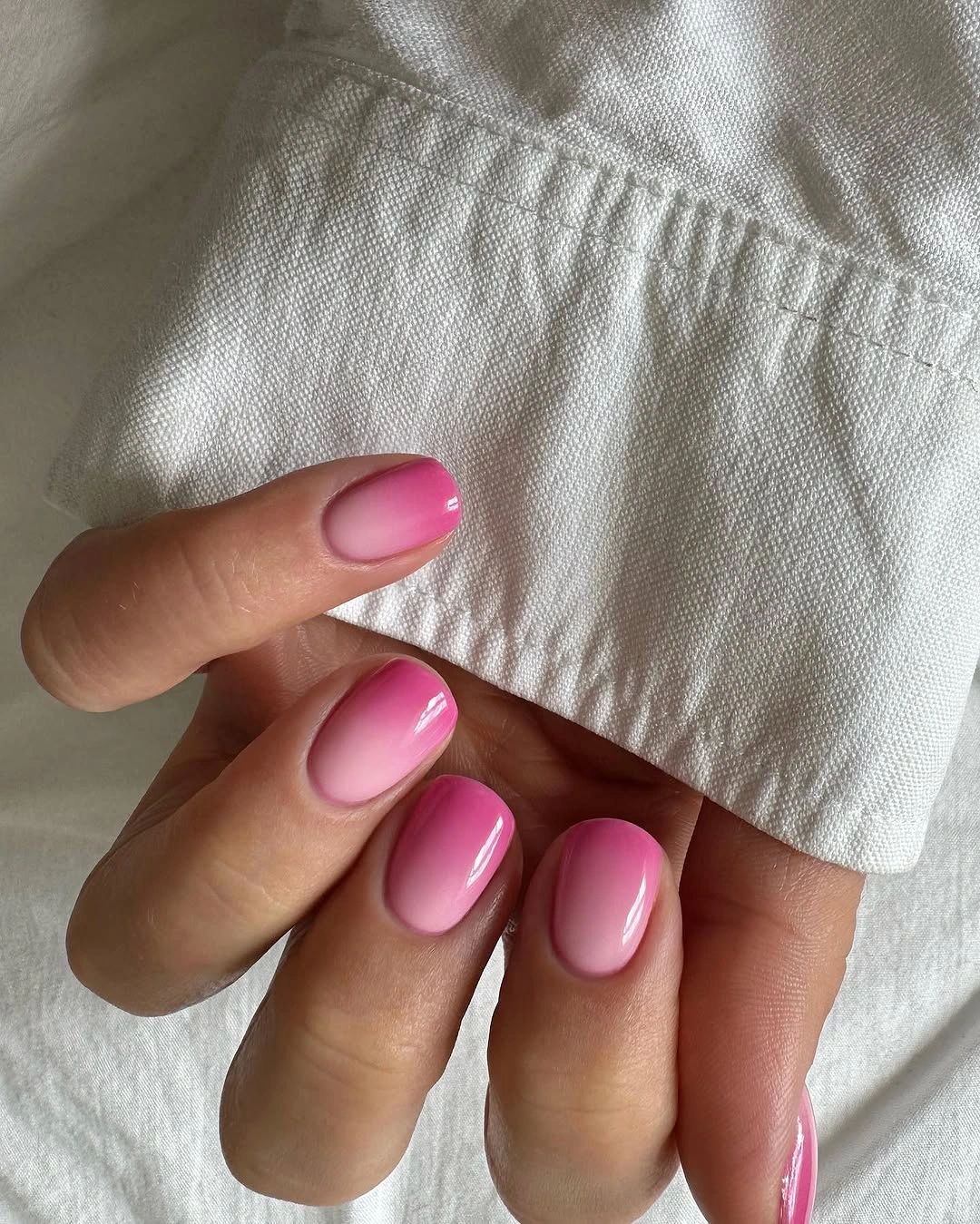 Glossy pink oval nails under white fabric