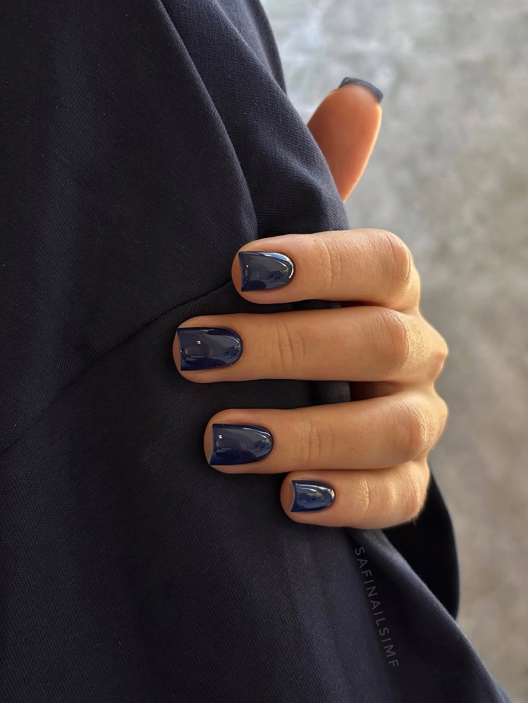 Glossy navy short nails against dark fabric