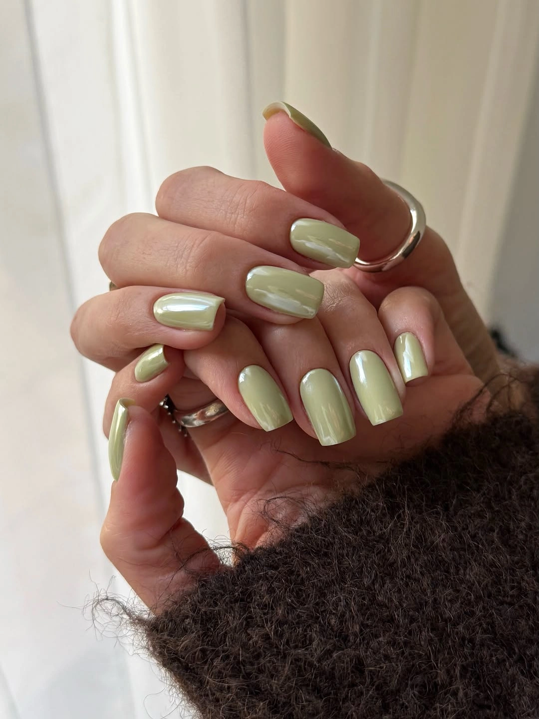 Short glossy olive nails beside a fuzzy dark sleeve