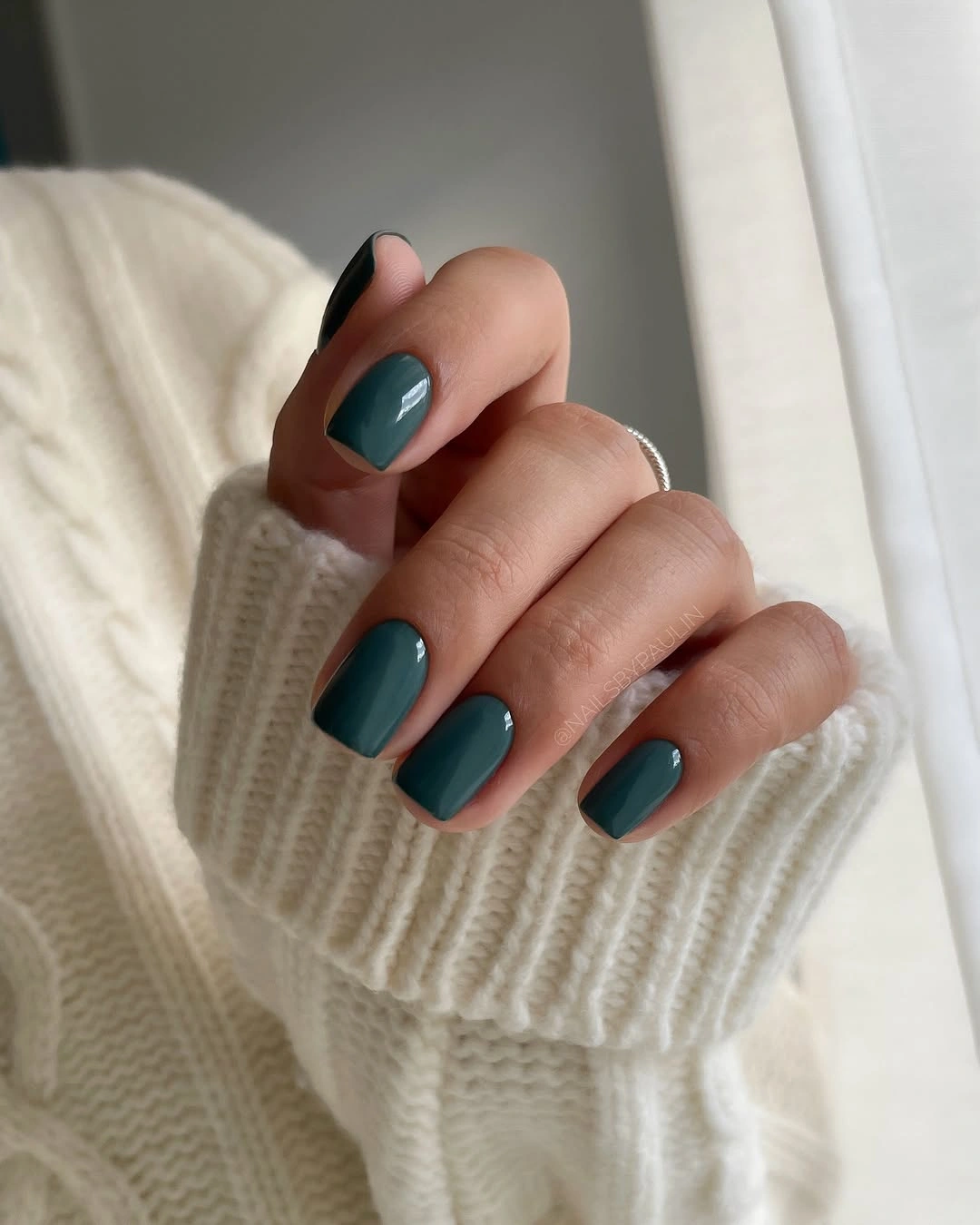 Short glossy teal nails with a cream sweater