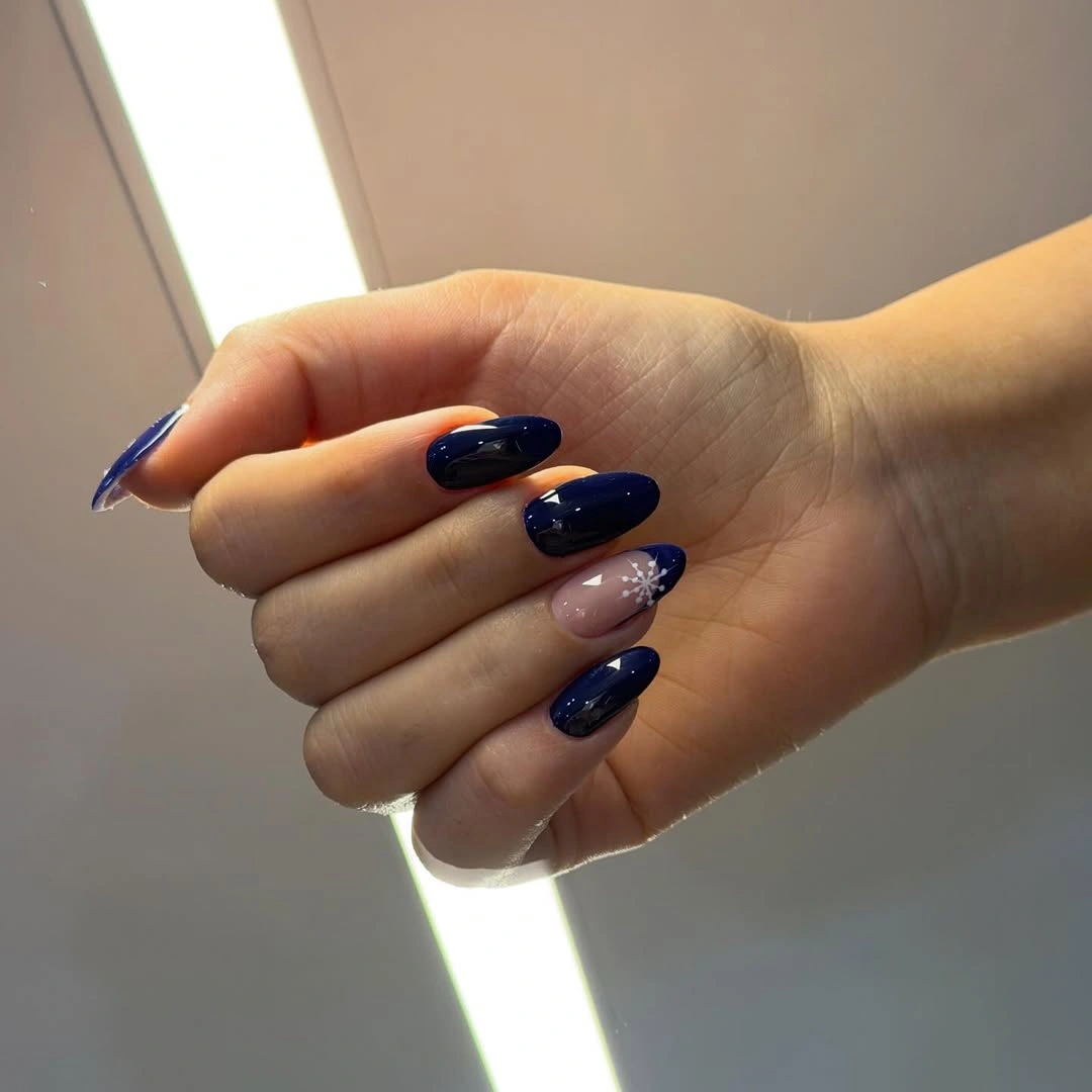 Glossy navy almond nails with one pale snowflake accent