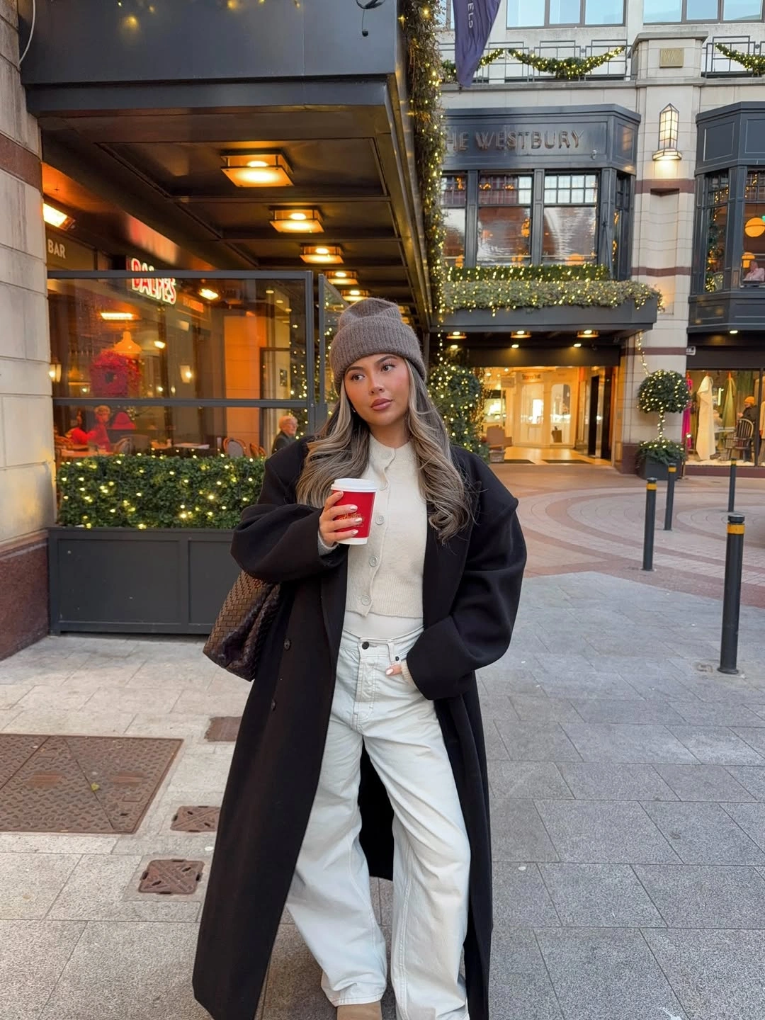 Black coat with ivory cardigan, pale jeans and woven brown bag