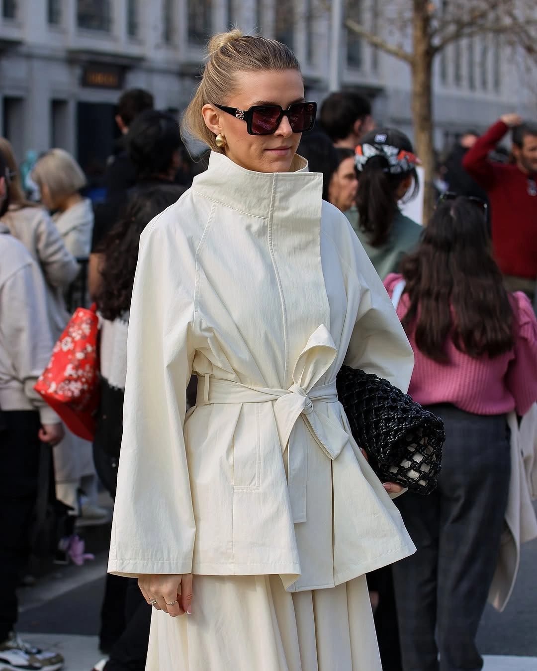 Cream belted high-collar jacket with dark clutch and sunglasses