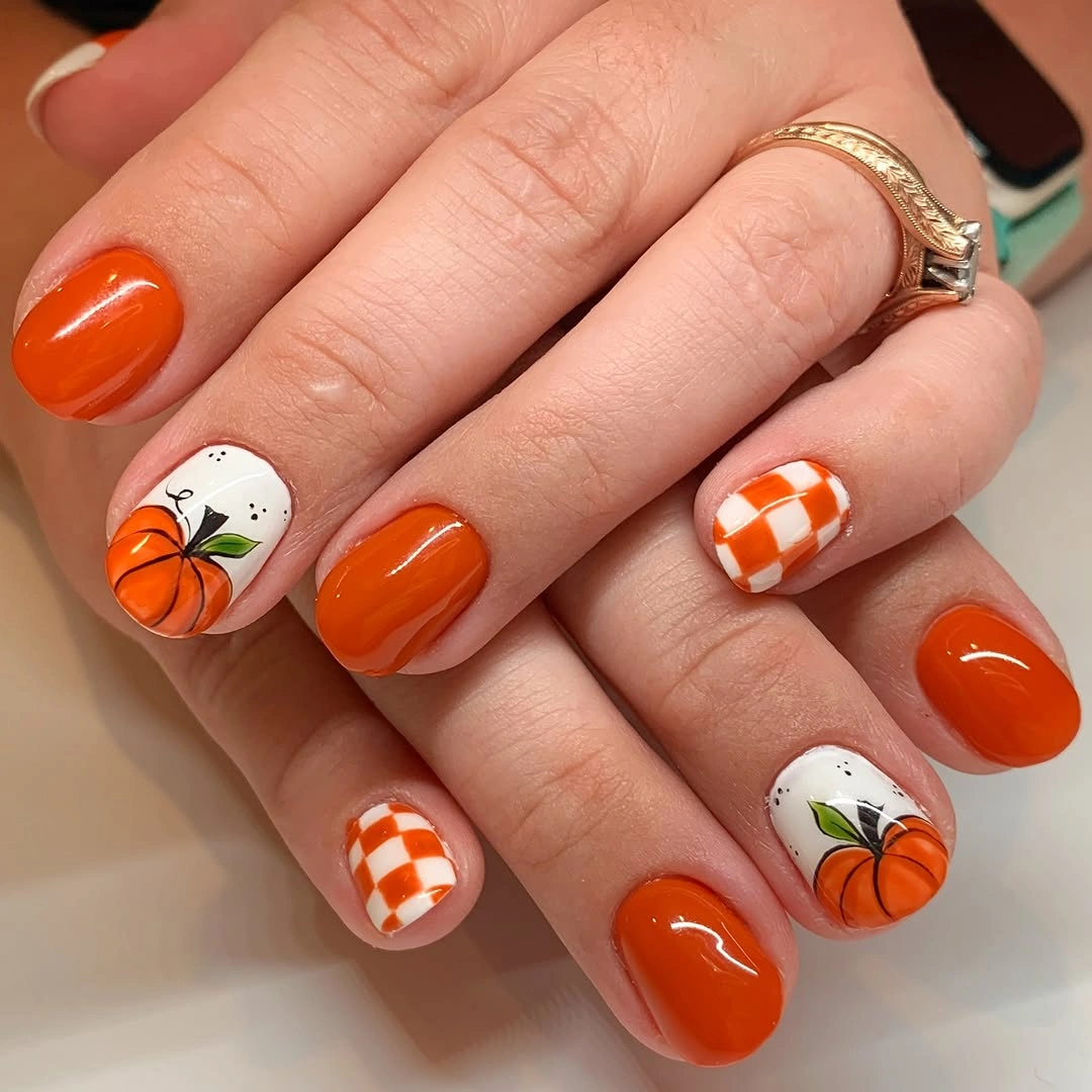Glossy orange rounded nails with pumpkin and checker accents
