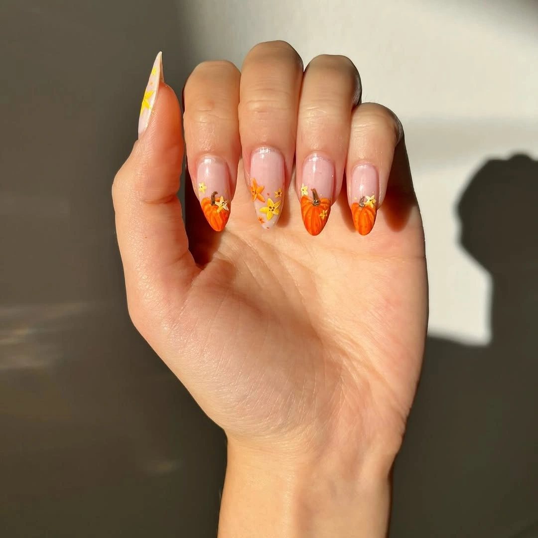 Nude almond nails with orange tips and tiny pumpkins