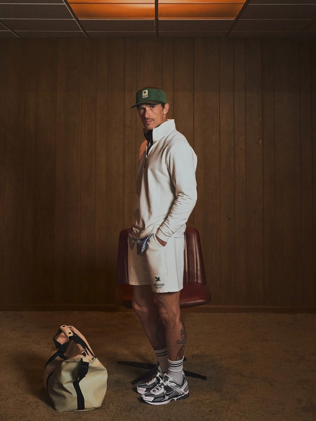 Man in pale quarter-zip set, green cap and striped socks