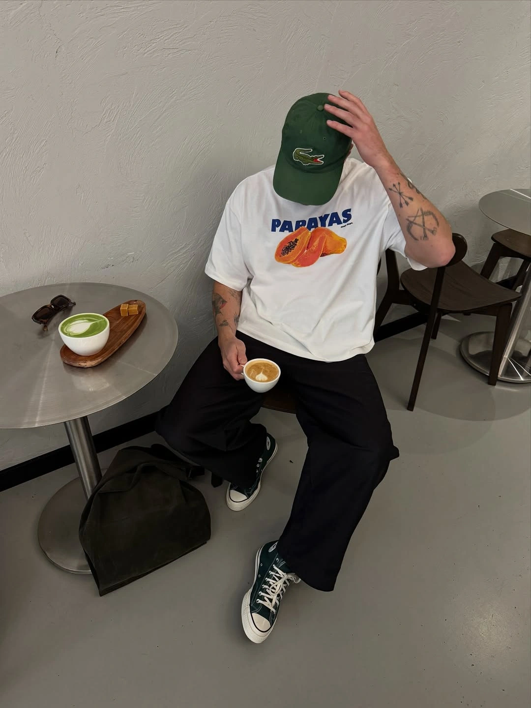 Seated man in papaya graphic tee and green high-top sneakers