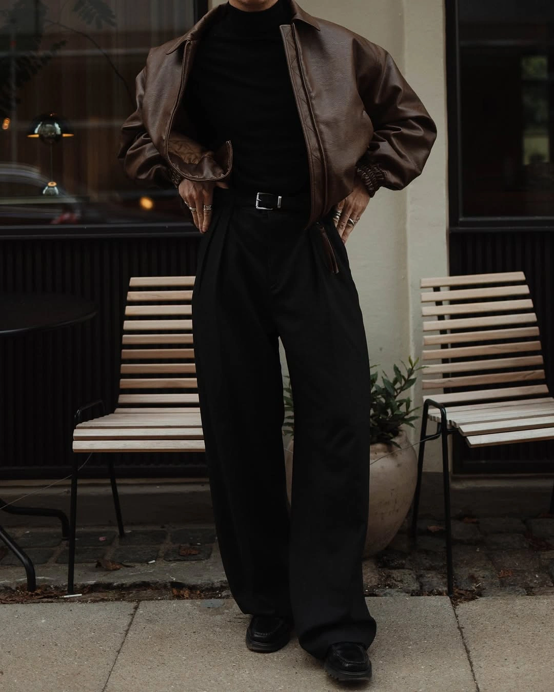 Cropped figure in chocolate bomber, black trousers and silver belt buckle