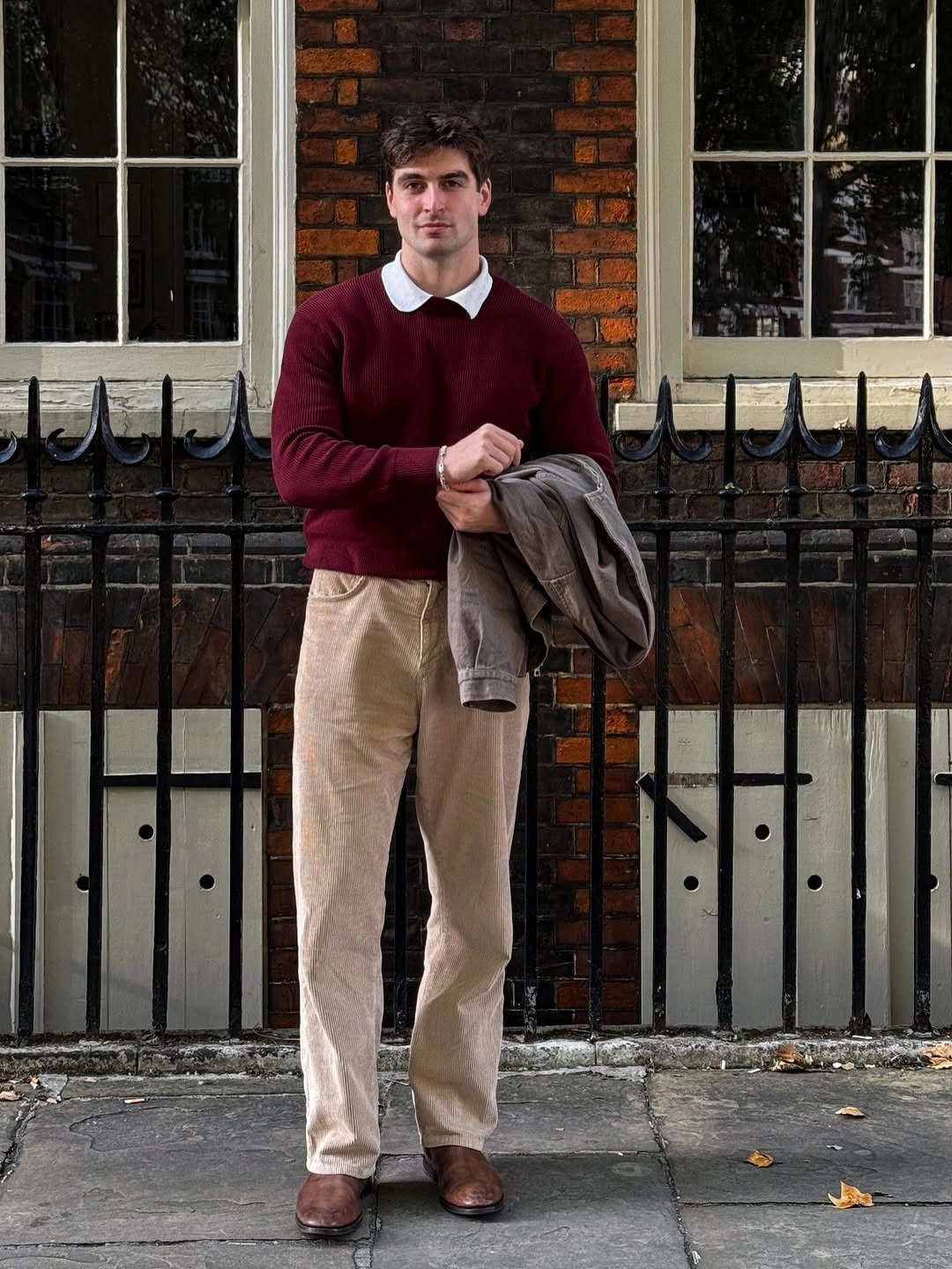 Man in burgundy sweater, white collar and pale ridged trousers