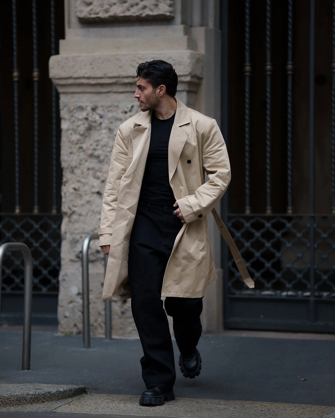 Man in beige trench-style coat over black shirt and trousers