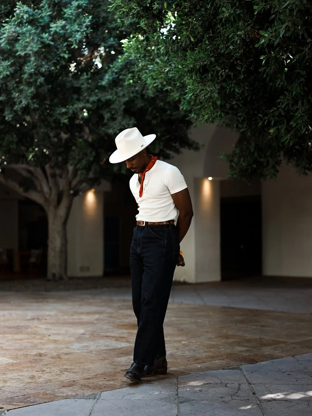 Man in white hat, white top, red-orange scarf and dark trousers
