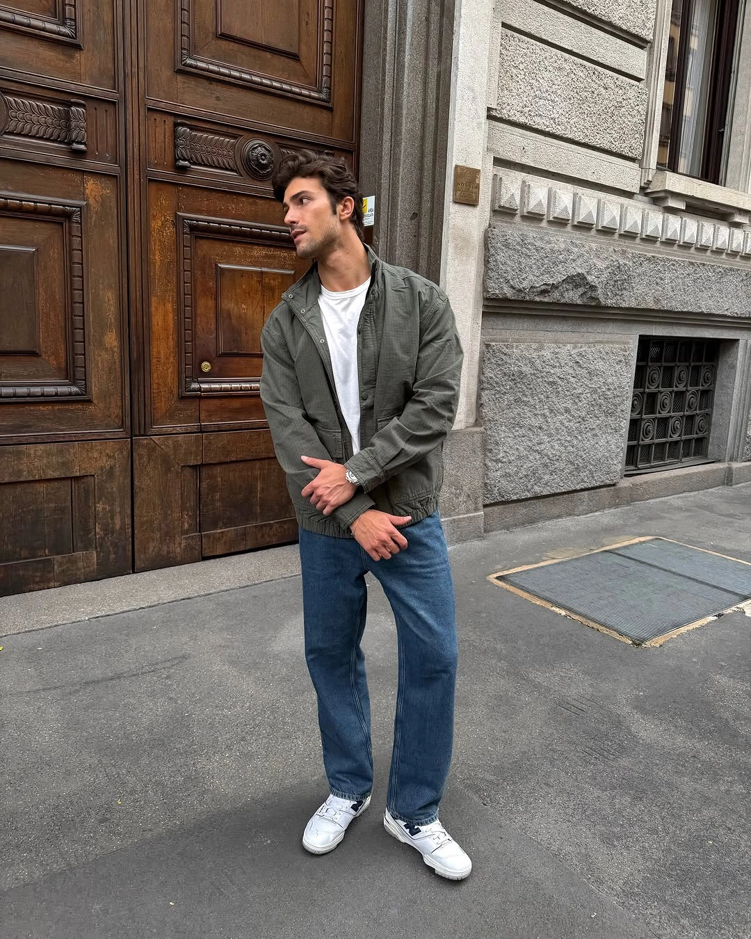Man in olive jacket, white tee, blue jeans and sneakers