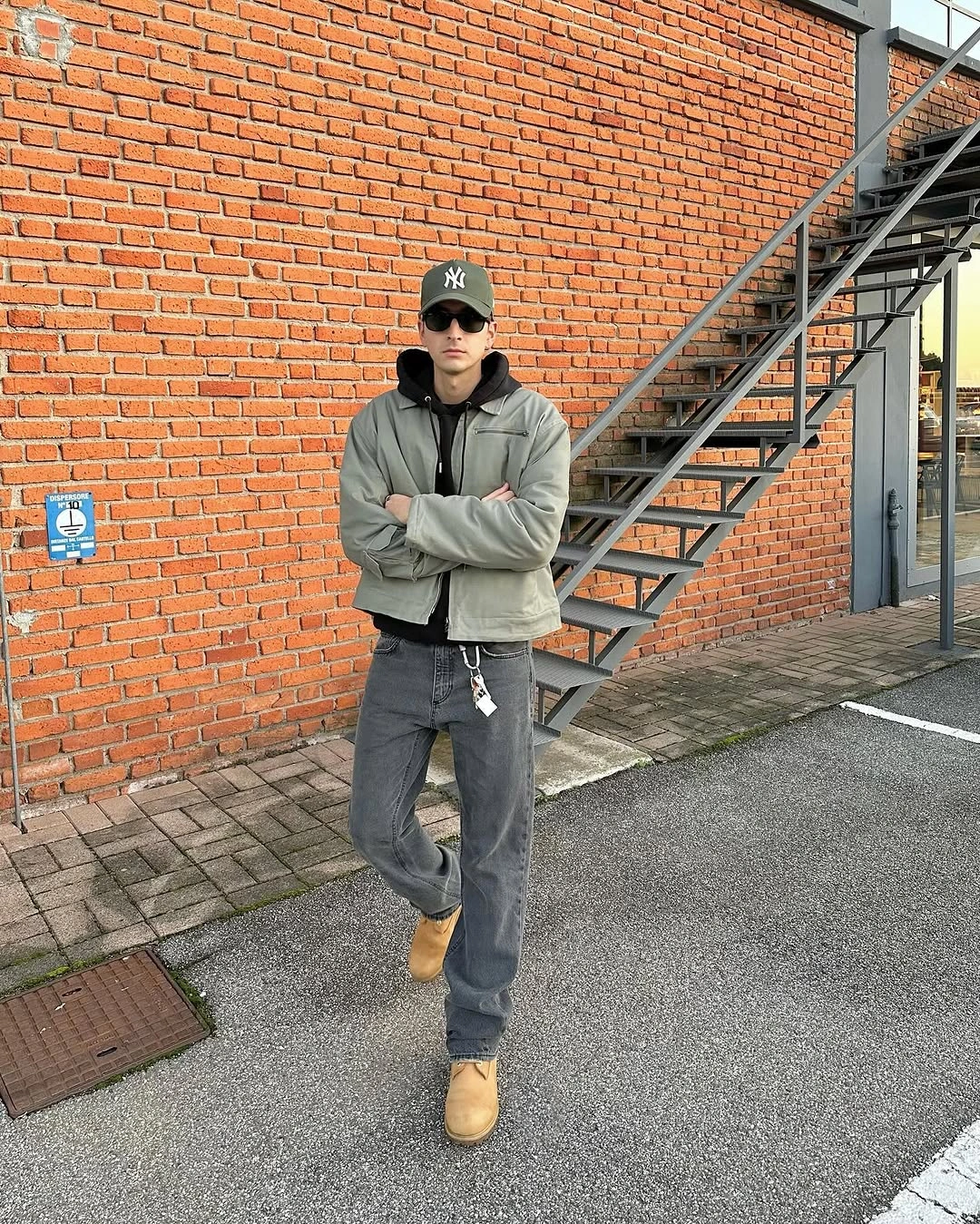 Man in gray-green jacket, black hoodie, gray jeans and tan boots
