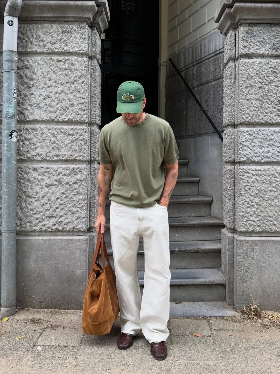 Man in olive knit top, white trousers and tan tote