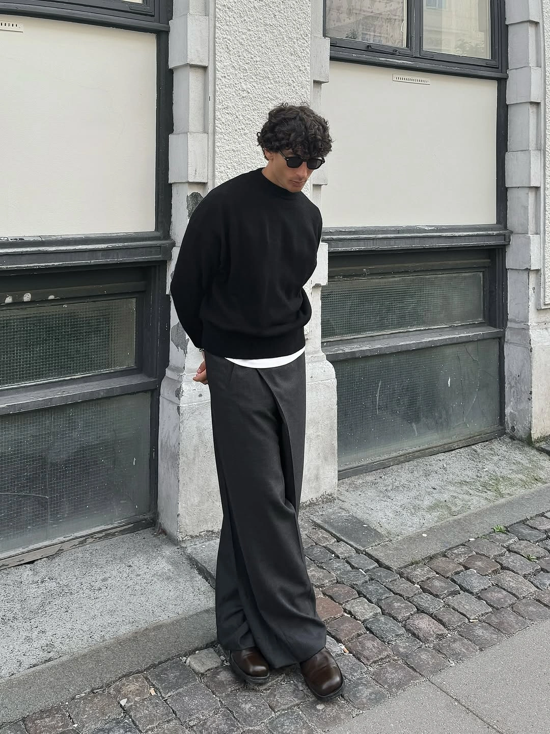 Man in oversized black top, charcoal trousers and brown shoes