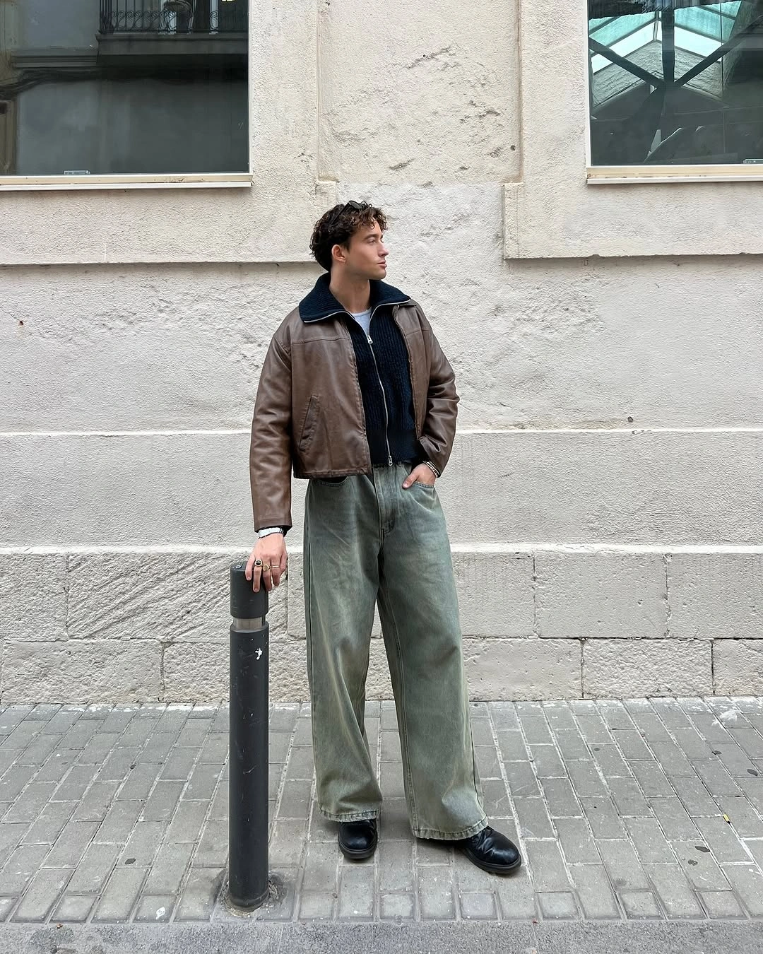 Man in brown cropped jacket and muted green wide jeans