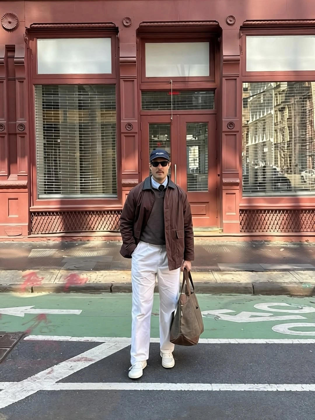Man in brown jacket, charcoal sweater and white trousers