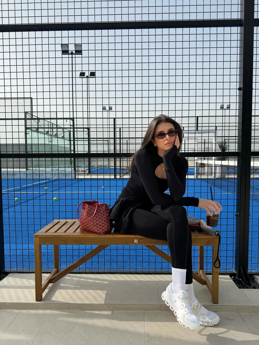 Black long sleeve padel outfit with white sneakers on blue court