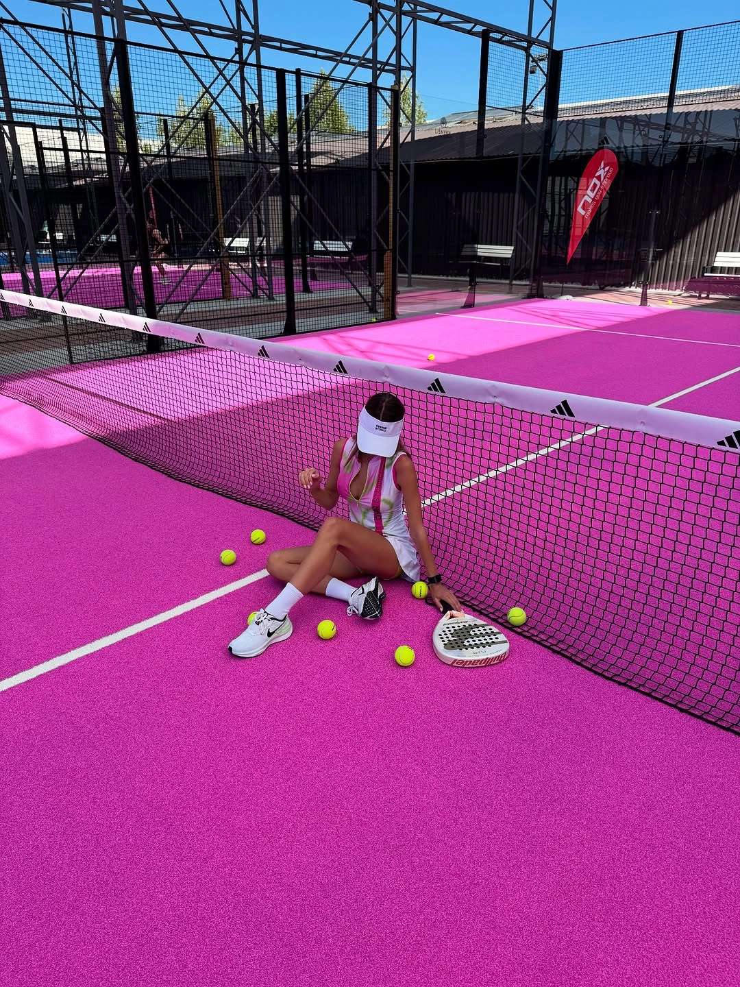 White sleeveless padel dress with visor on bright pink court