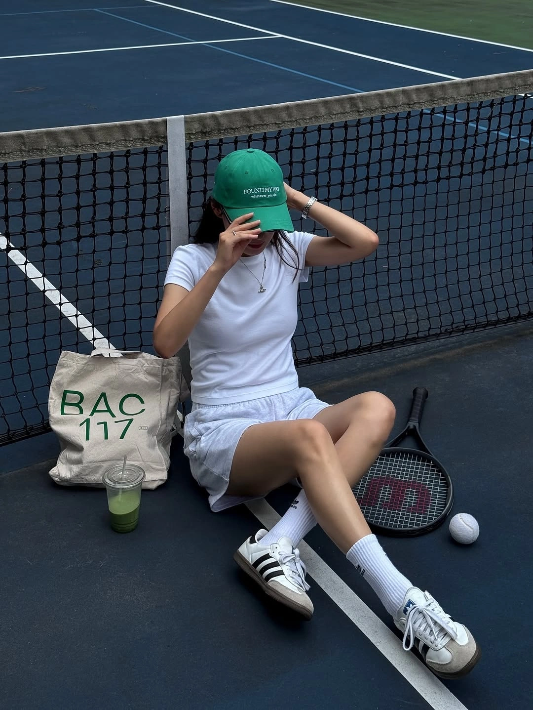White tee with gray shorts and green cap on dark court