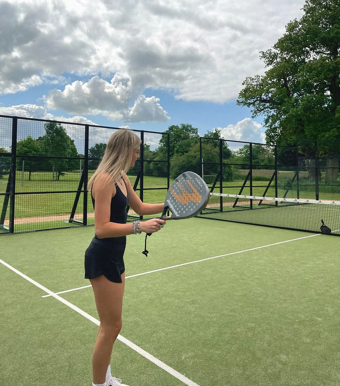 Dark strappy padel dress with orange racket outdoors