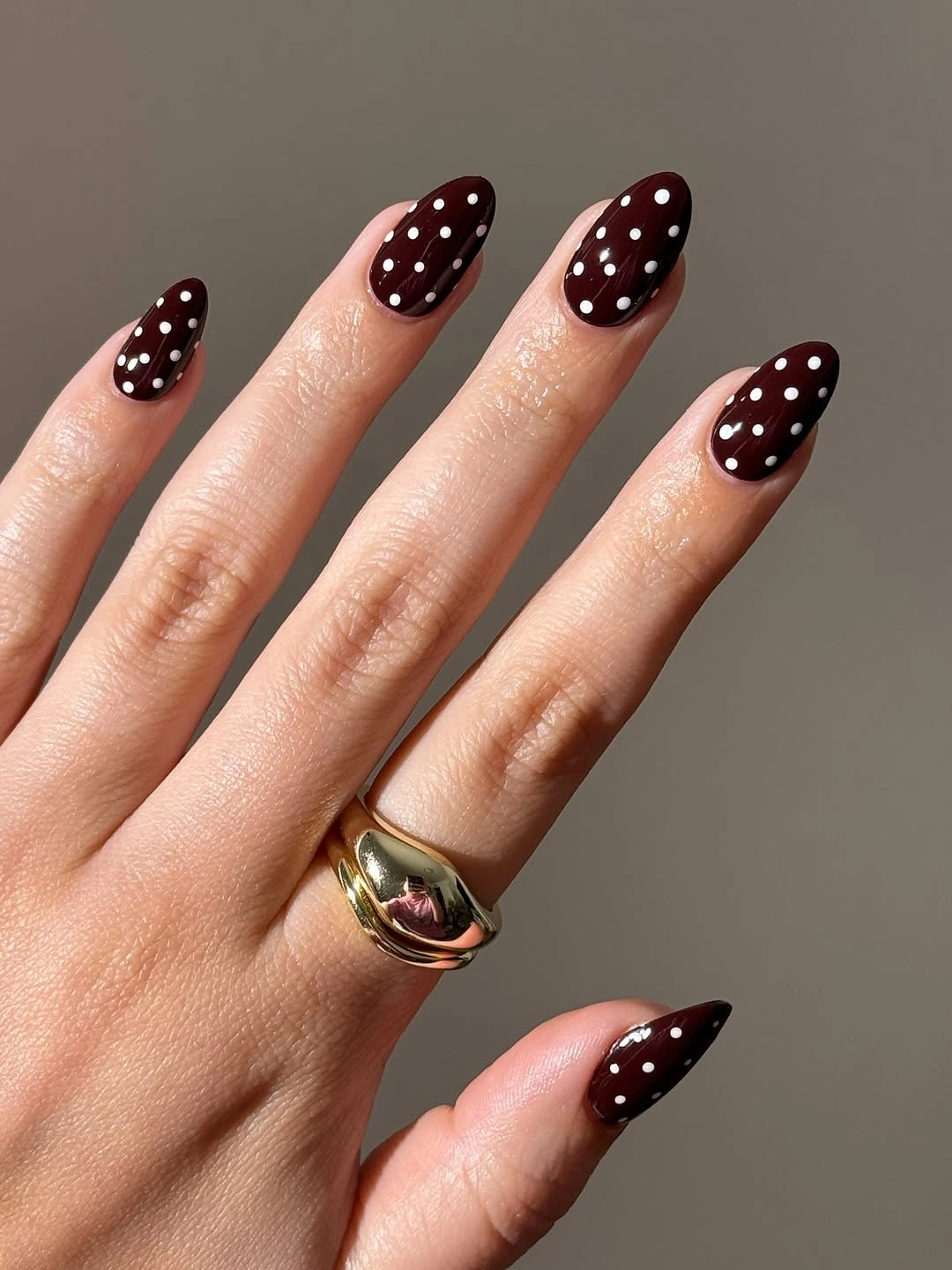 Deep burgundy almond nails covered in crisp white dots