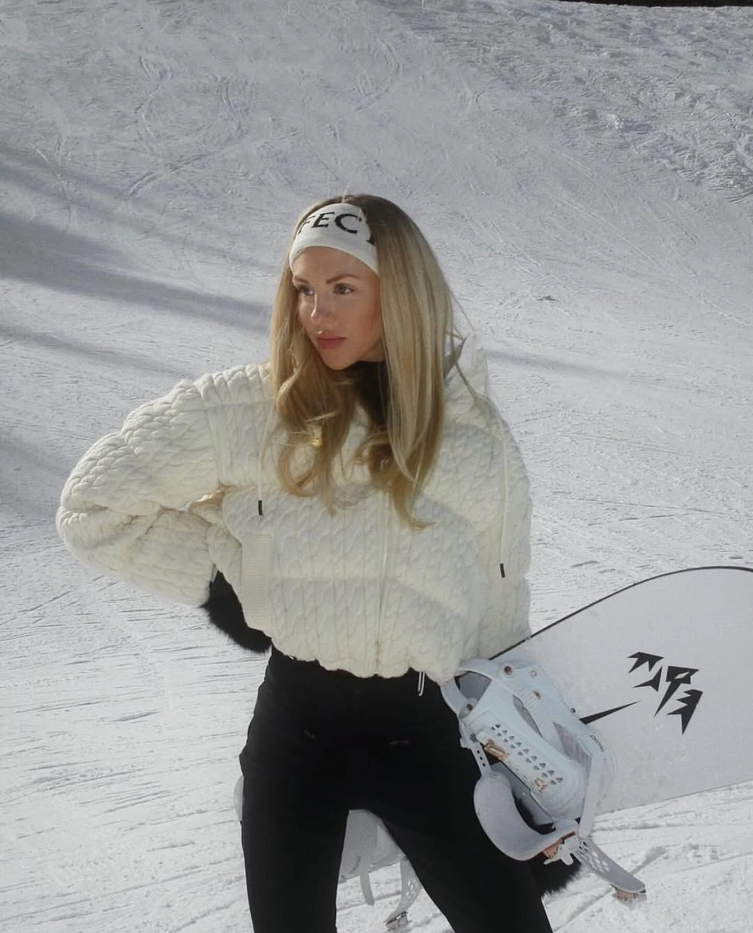 White quilted hooded jacket with black pants and snowboard