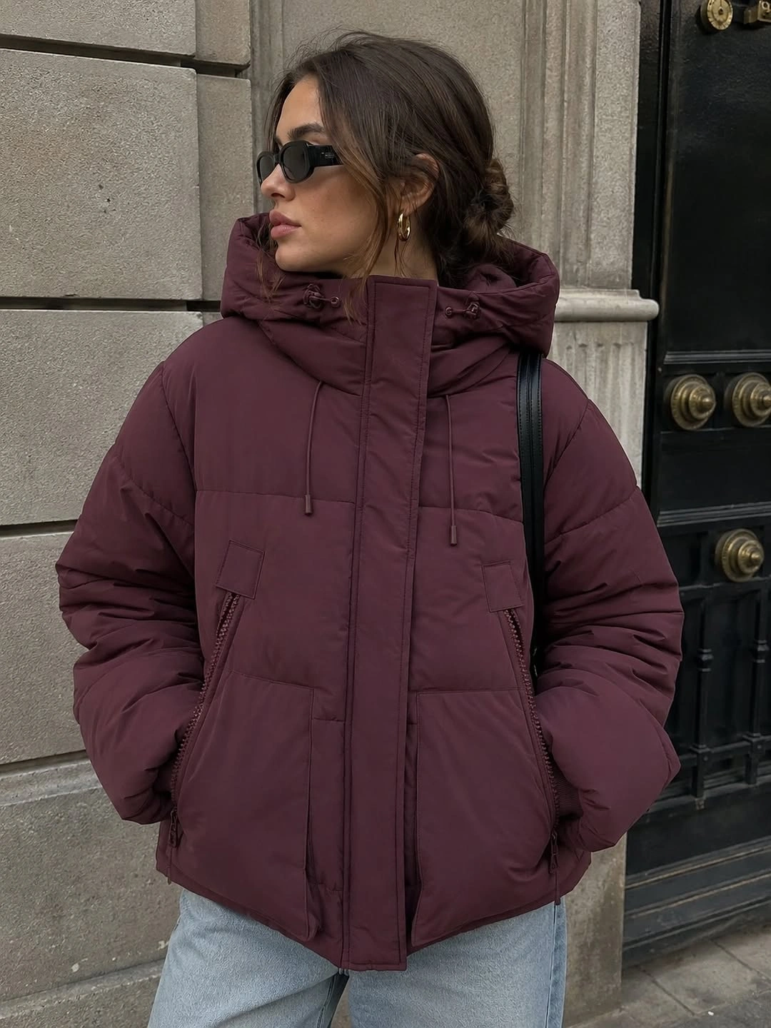 Burgundy hooded puffer with light jeans and black shoulder strap