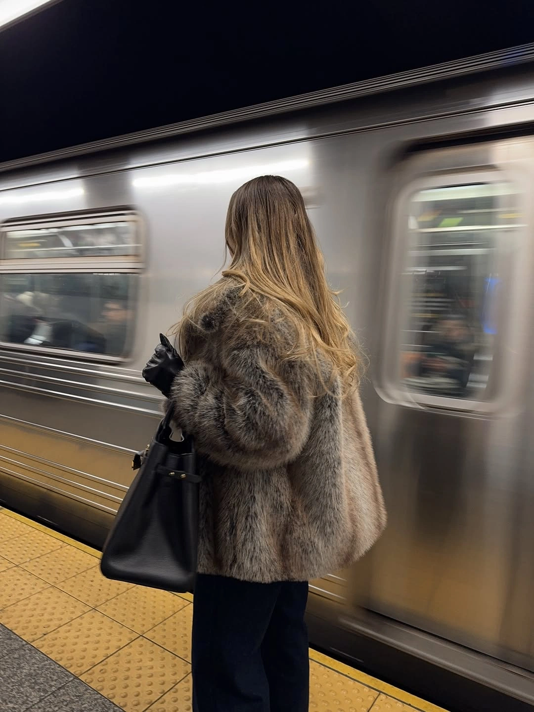 Shaggy gray-brown jacket with black bag beside subway train