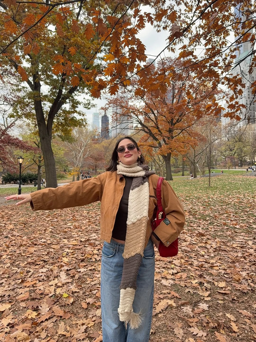 Tan jacket with long beige scarf, jeans and red shoulder bag