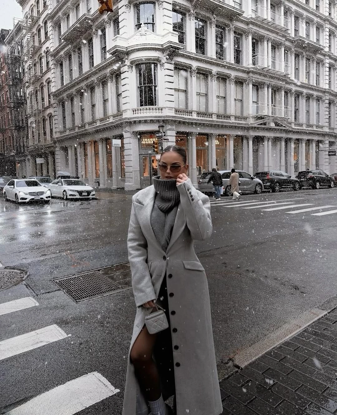 Gray tailored coat with dark hem, tights and small handbag